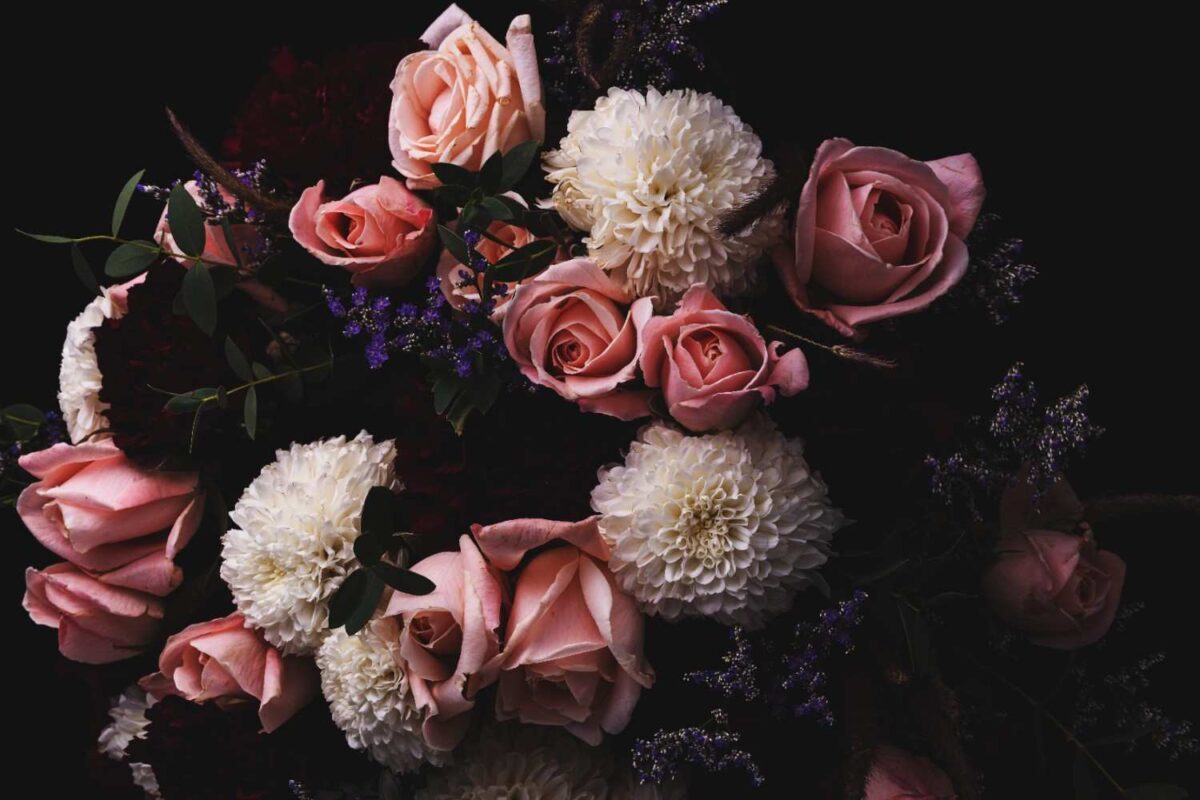 A closeup shot of luxurious flower bouquet including pink roses, white, red dahlias, and carnations.