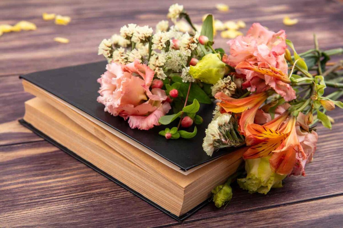 Side view of beautiful colorful graduation flowers with leaves on wooden surface with a book.